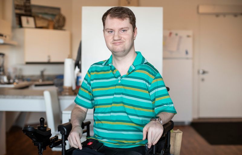 Levi Lawton seated in powerchair in his living room with kitchen behind.