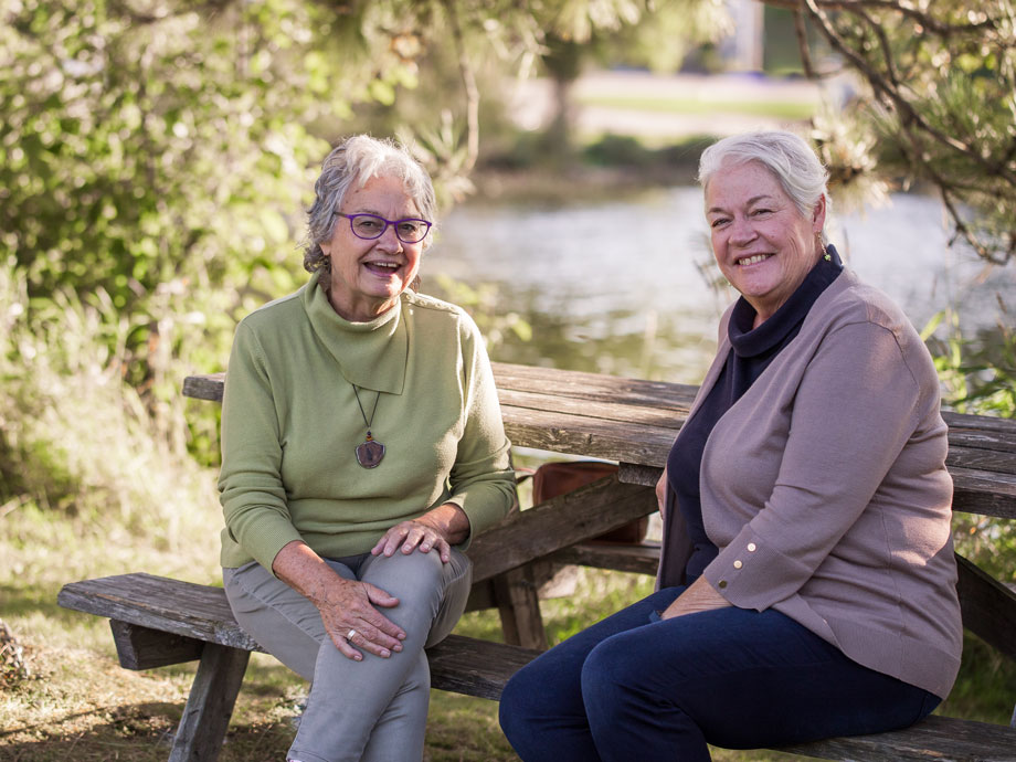 Fay Martin, founder, Places for People and president Jody Curry on a bench by a serene lake.