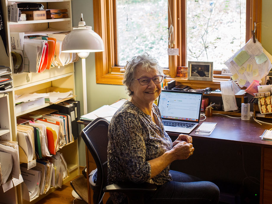 Fay sitting at her home office desk with an open laptop and a window behind her.